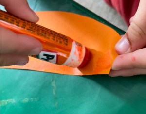 A childs hands using a small glue stick on an orange piece of paper