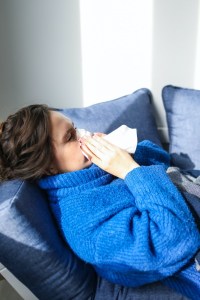 A woman in a blue jumper sneezes into a tissue