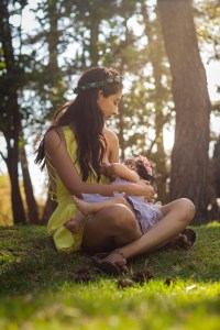 A woman in a green dress sits on the floor in the forest and breastfeeds an infant