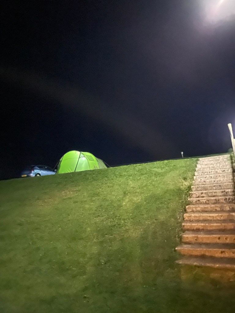 A green tent is illuminated on top of a grass hill against a dark sky at a caravan parks near Whitby 