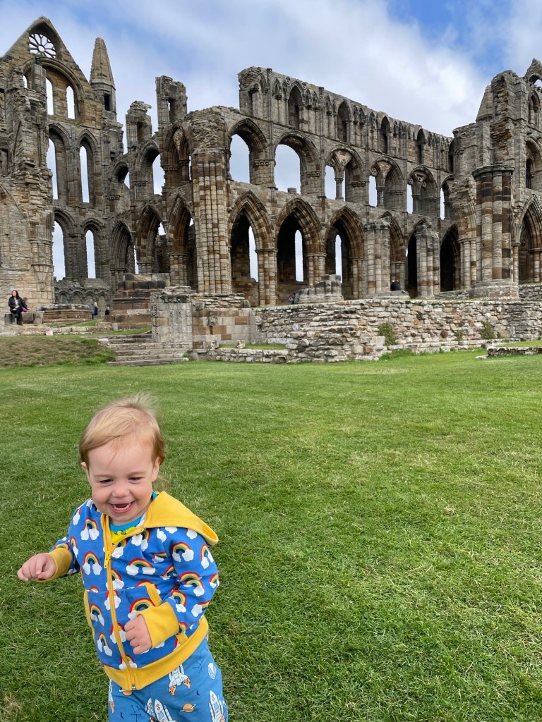 A child runs laughing in front of Whitby Abbey