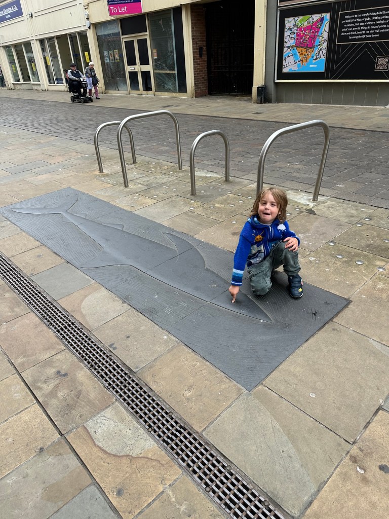 a boy is kneeling down to point to a shark image on the pavement of the fish trail in hull